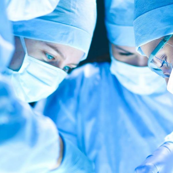 4 Ärzte in bleuer Kleidung mit Mundschutz operieren